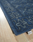 Mira Traditional Blue Hand Knotted Wool Rug, displays a complex, geometric pattern in varying shades of blue, ivory, and hints of red, lending a sophisticated touch to the warmly lit living room setting.