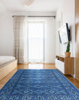 Mira Traditional Blue Hand Knotted Wool Rug, a richly patterned floor covering with deep blues and intricate detailing, adds warmth and elegance to a softly lit room with hardwood floors and neutral walls.
