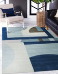 Bespoke Iris Multicolor Hand Tufted Wool Rug sprawls across a light-wood floor in a warmly lit interior; vibrant hues of blues, purples, greens, and yellows bloom across its hand-tufted wool surface, creating an inviting, textured focal point.