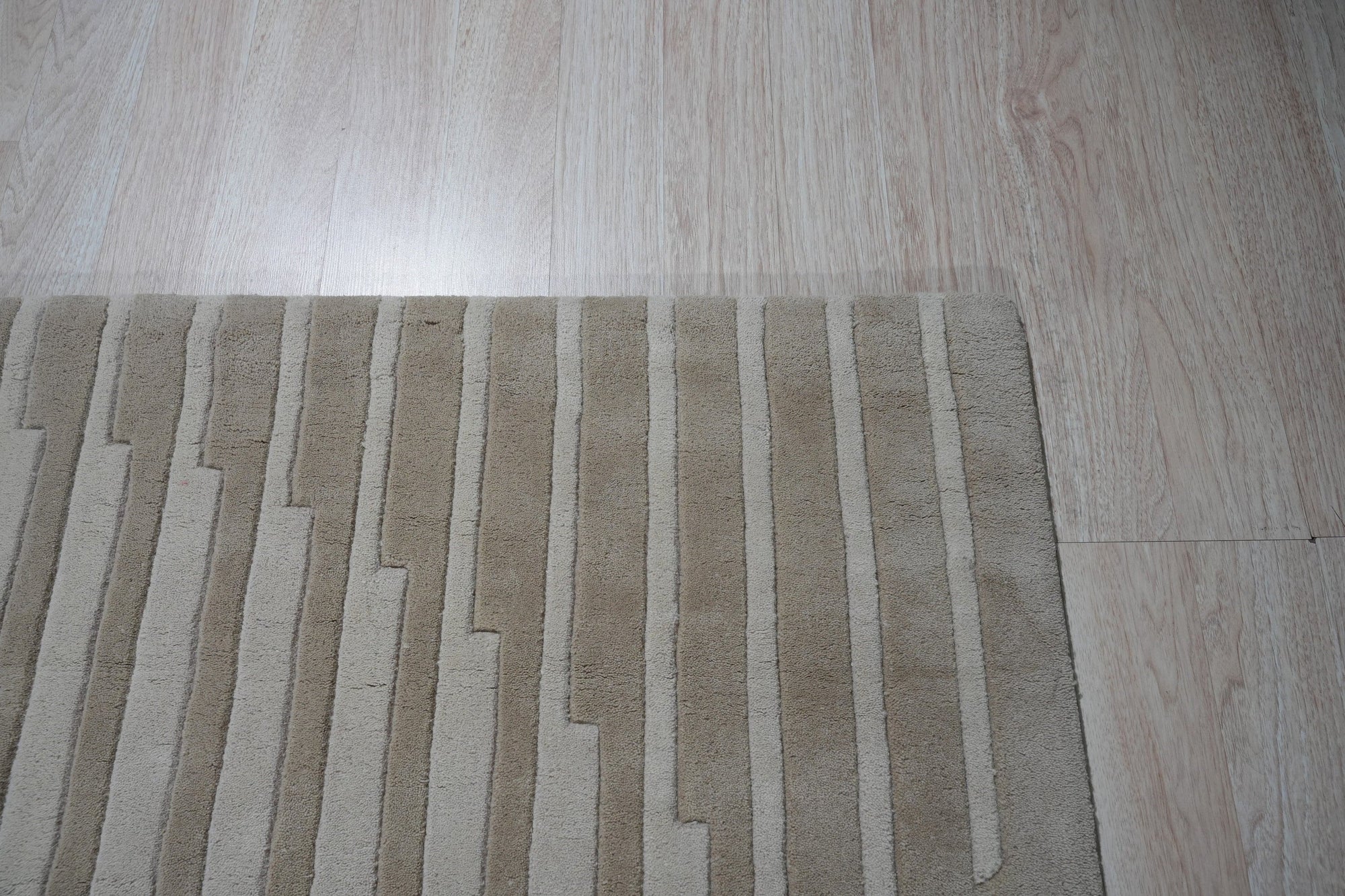 Maya Bianca Beige Hand Tufted Wool Rug, soft beige and ivory tones creating a subtle geometric pattern, graces a warmly lit interior space.