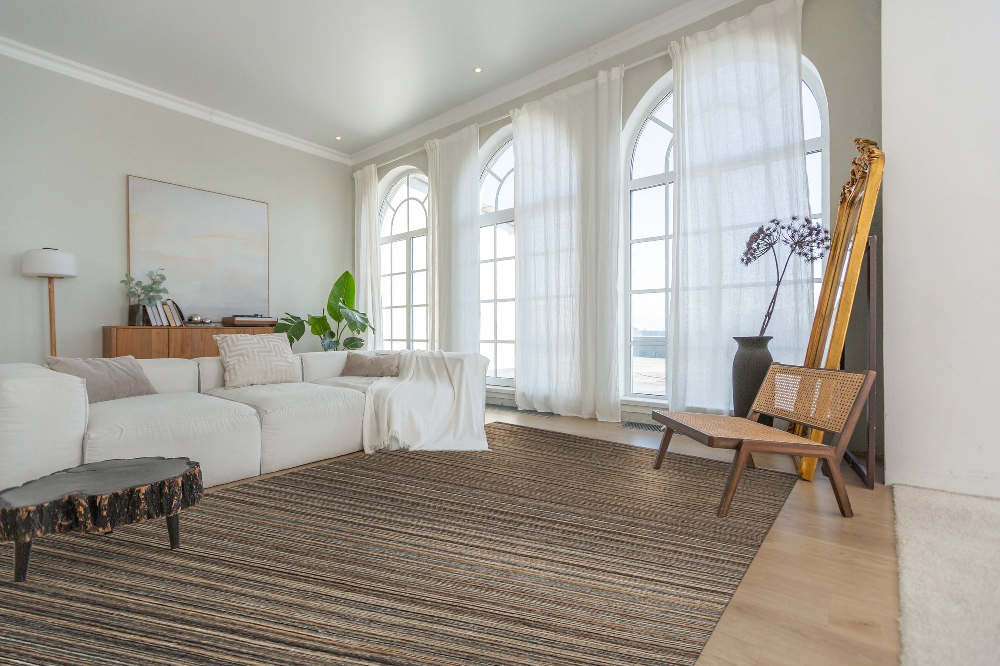 Artisan Striped Rust Handmade Rug features warm rust, beige, and cream stripes in a textured, hand-woven design, grounding a modern living room with hardwood floors and a neutral sofa.