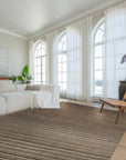 Artisan Striped Rust Handmade Rug features warm rust, beige, and cream stripes in a textured, hand-woven design, grounding a modern living room with hardwood floors and a neutral sofa.