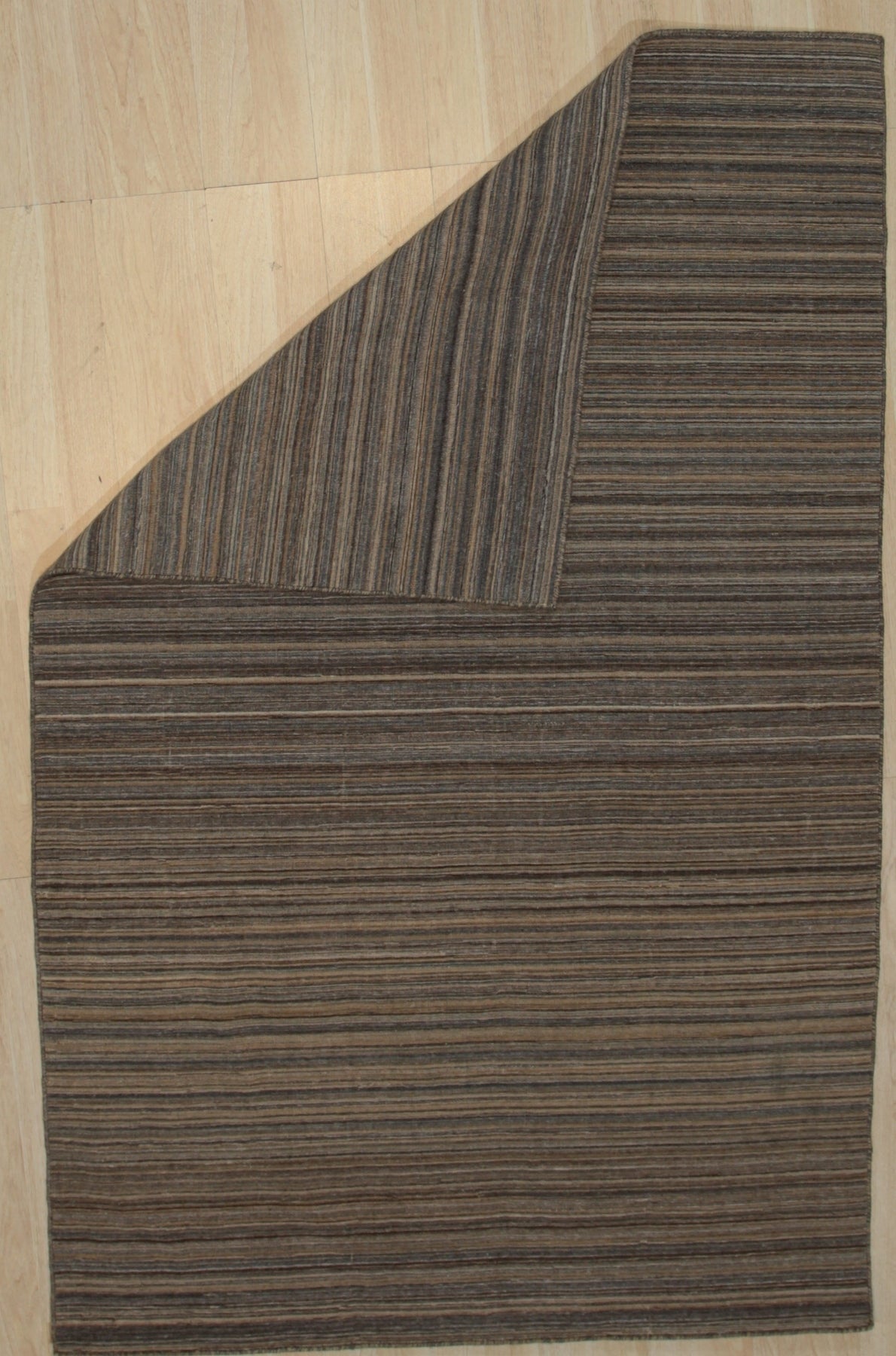 Artisan Striped Rust Handmade Rug displayed in a bright, airy living room. Warm rust and cream stripes add a touch of rustic charm to the space, complementing the wooden furniture and natural light. The handwoven texture suggests quality craftsmanship and cozy comfort.