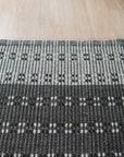 Clara Xena Charcoal Flatweave Wool & Cotton Rug, its textured weave and subtle charcoal hues grounding a modern living room with natural light and minimalist furniture.