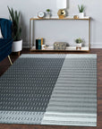 Clara Xena Charcoal Flatweave Wool & Cotton Rug displayed in a bright living room setting. Neutral walls and warm wood furniture complement the rug’s subtle charcoal tones and flatweave construction, creating a comfortable, inviting space.