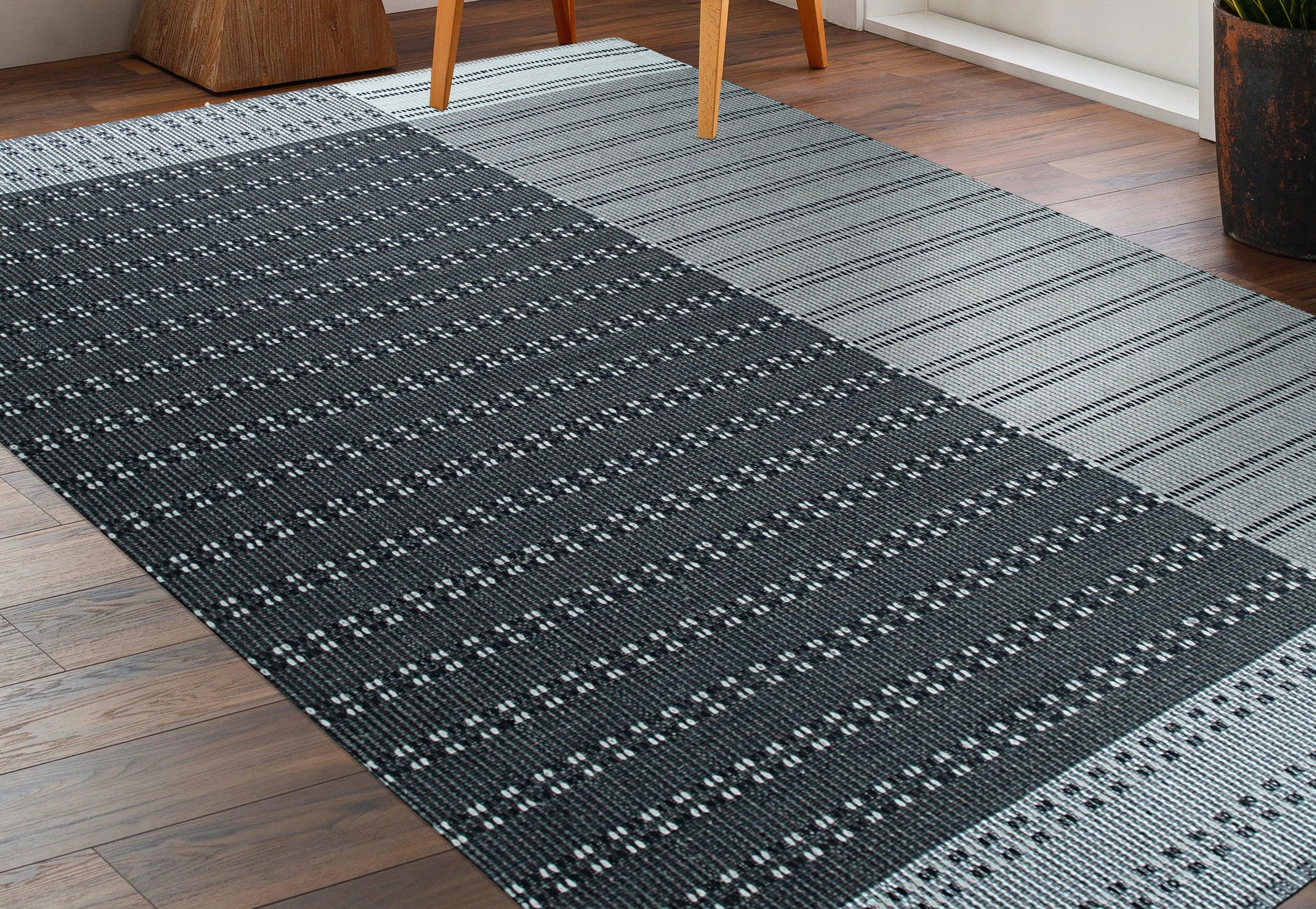 Clara Xena Charcoal Flatweave Wool & Cotton Rug, a charcoal and ivory patterned rug, anchors a modern living room with a light wood coffee table and cozy throw pillows.