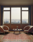 Celia Oushak Rust Hand Knotted Wool Rug, displayed on a polished hardwood floor. Warm rust tones and intricate Oushak patterns dominate the hand-knotted wool surface, creating a vibrant and inviting atmosphere.