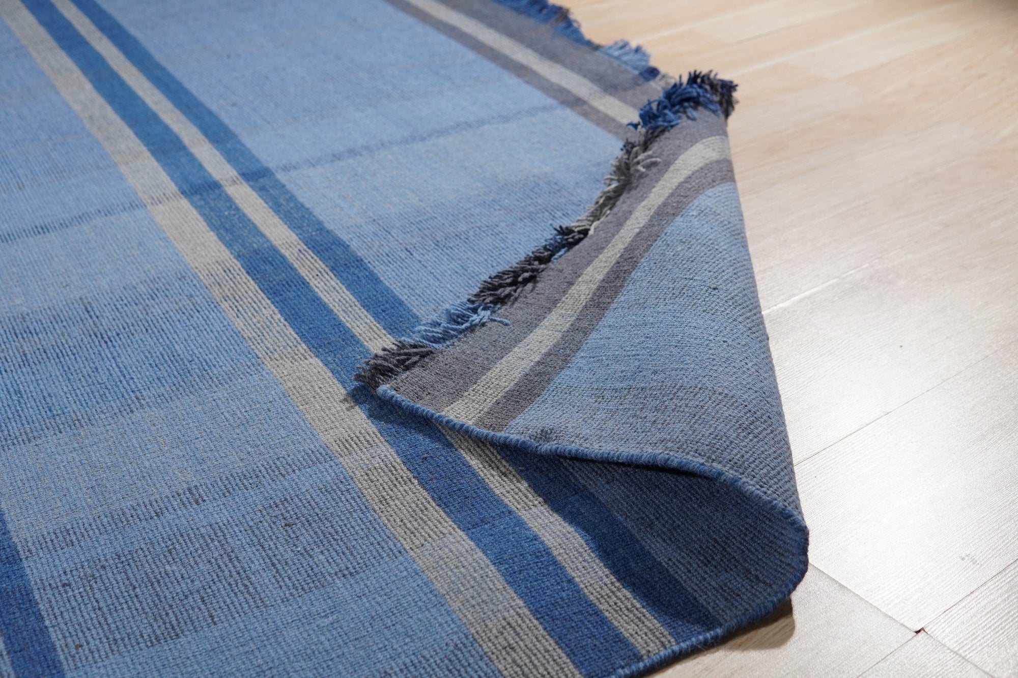 Maya Opulent Blue Flatweave Wool Rug, showcasing a richly textured surface in varying shades of blue, its flatweave construction lending a modern, understated elegance in a well-lit room.