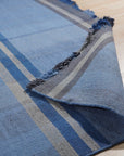 Maya Opulent Blue Flatweave Wool Rug, showcasing a richly textured surface in varying shades of blue, its flatweave construction lending a modern, understated elegance in a well-lit room.