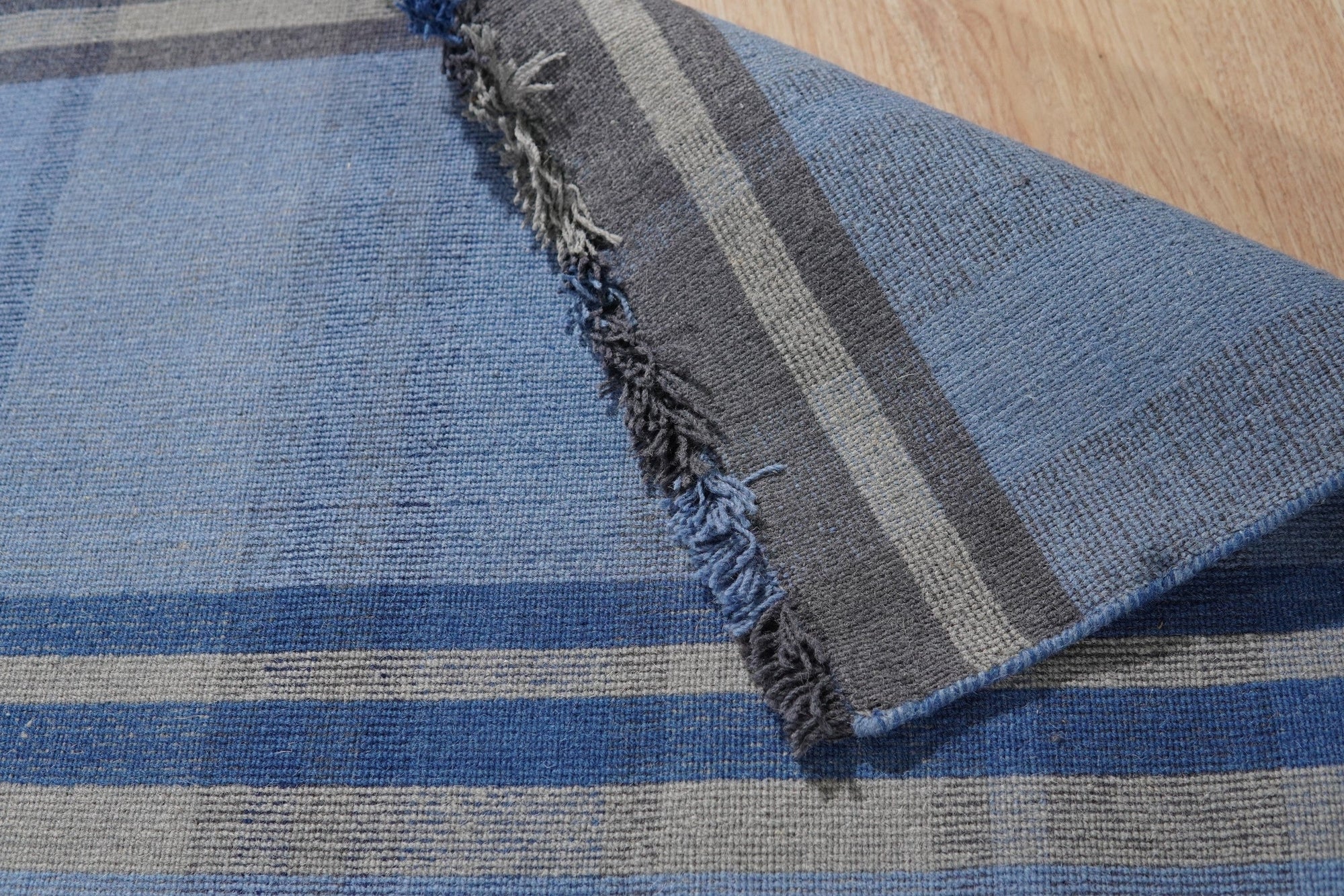 Maya Opulent Blue Flatweave Wool Rug, displaying its intricate pattern and rich blue hues, rests on a light hardwood floor in a brightly lit room, suggesting a stylish and comfortable living space.