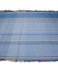 Maya Opulent Blue Flatweave Wool Rug, blending cool blue hues in a flatweave construction, graces a contemporary living space with minimalist furniture and warm lighting.