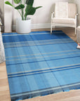Maya Opulent Blue Flatweave Wool Rug, sprawling across a bright room, its geometric patterns in blues and creams adding a touch of modern sophistication to the light wood floor.