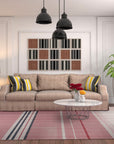 Maya Giselle Pink Flatweave Wool Rug, a delicate ballet of blush pink and soft ivory, sprawls across a warmly lit living room, its flatweave construction adding subtle texture beneath inviting mid-century modern furniture.