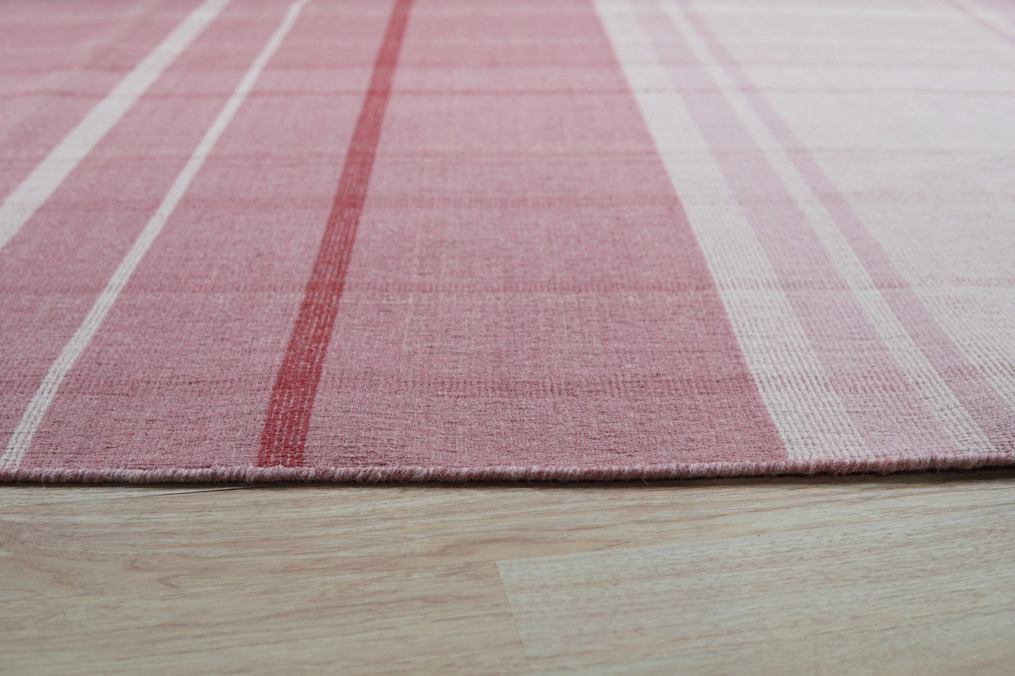 Maya Giselle Pink Flatweave Wool Rug, a flatweave wool rug in soft pink tones, lies on a light wood floor, showcasing its delicate texture and subtle geometric pattern in a bright, modern room.