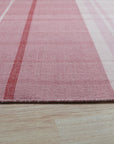 Maya Giselle Pink Flatweave Wool Rug, a flatweave wool rug in soft pink tones, lies on a light wood floor, showcasing its delicate texture and subtle geometric pattern in a bright, modern room.