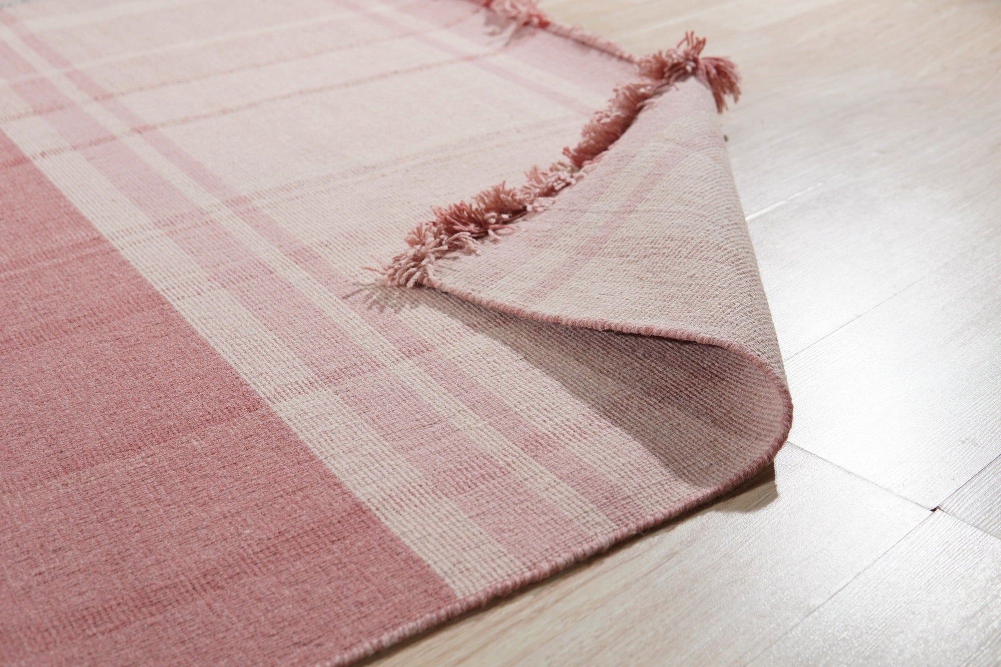 Maya Giselle Pink Flatweave Wool Rug, a blush pink and ivory flatweave wool rug with a subtle geometric pattern, shown in a bright living room setting.