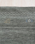 Freya Gabbeh Gray Handmade Wool Rug displayed on a light hardwood floor. Soft, undyed wool variations in cool gray create a minimalist, textured surface, showcasing the rug's hand-knotted construction and subtle geometric pattern.