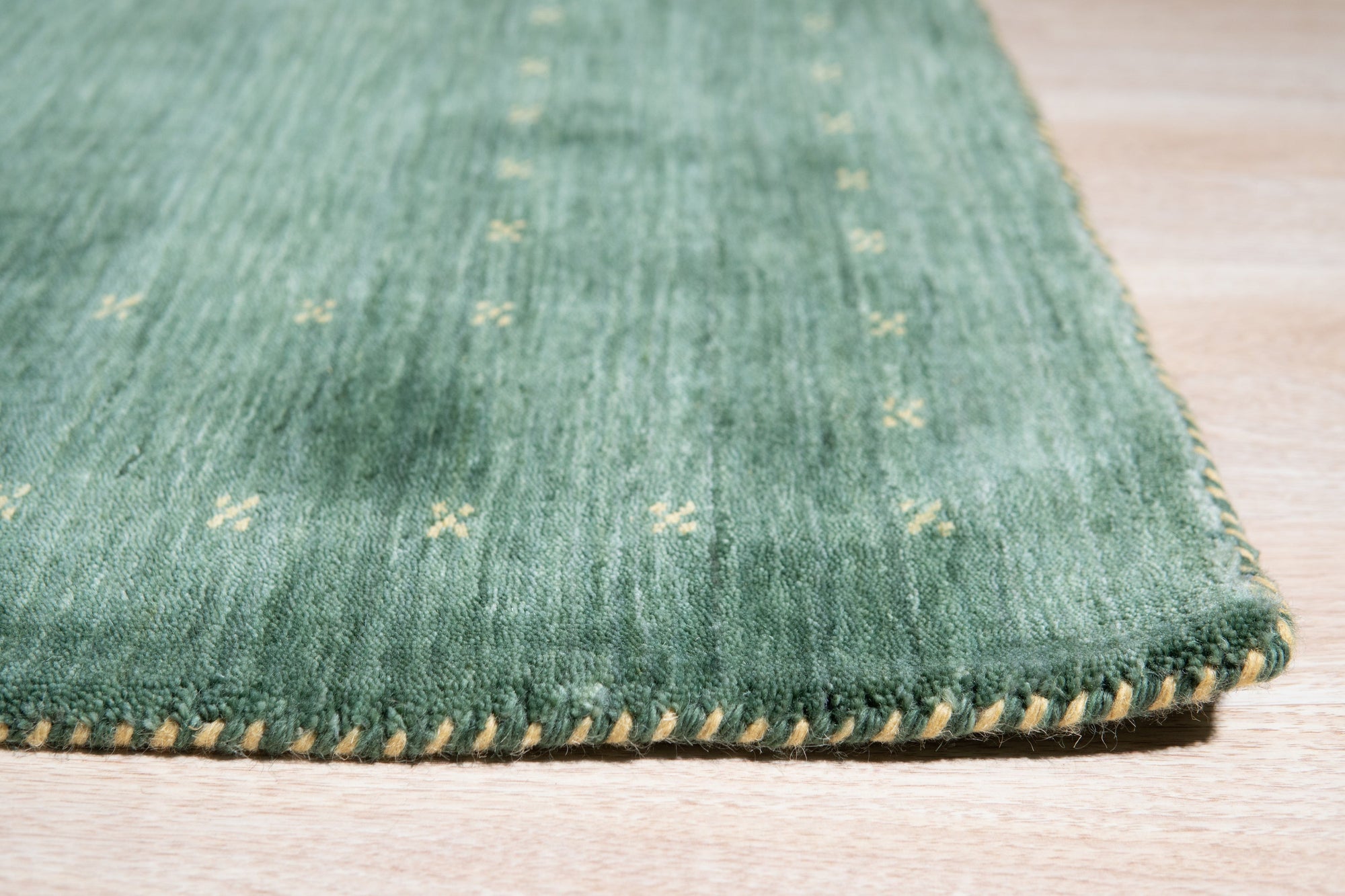 Sloane Ava Green Handmade Wool Rug, showcasing a modern living room setting with a light wood coffee table atop the green and cream patterned rug.
