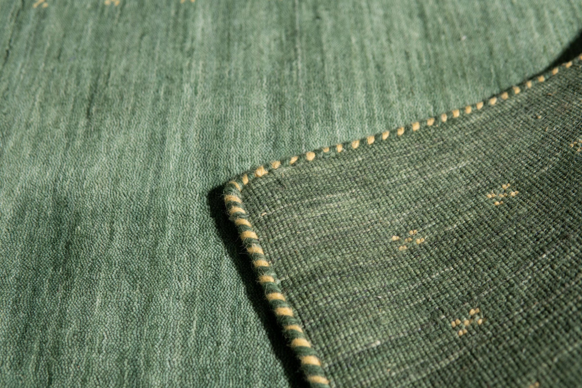 Sloane Ava Green Handmade Wool Rug, a lush expanse of emerald and sage wool, textures subtly shifting under dappled light. This handmade rug, with its nuanced green hues, anchors a relaxed living space featuring natural wood furniture and neutral textiles.