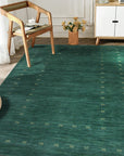 Sloane Ava Green Handmade Wool Rug, luxurious wool floor covering, features a muted green palette with subtle variations, its handmade construction adding depth and texture to a softly lit interior space.