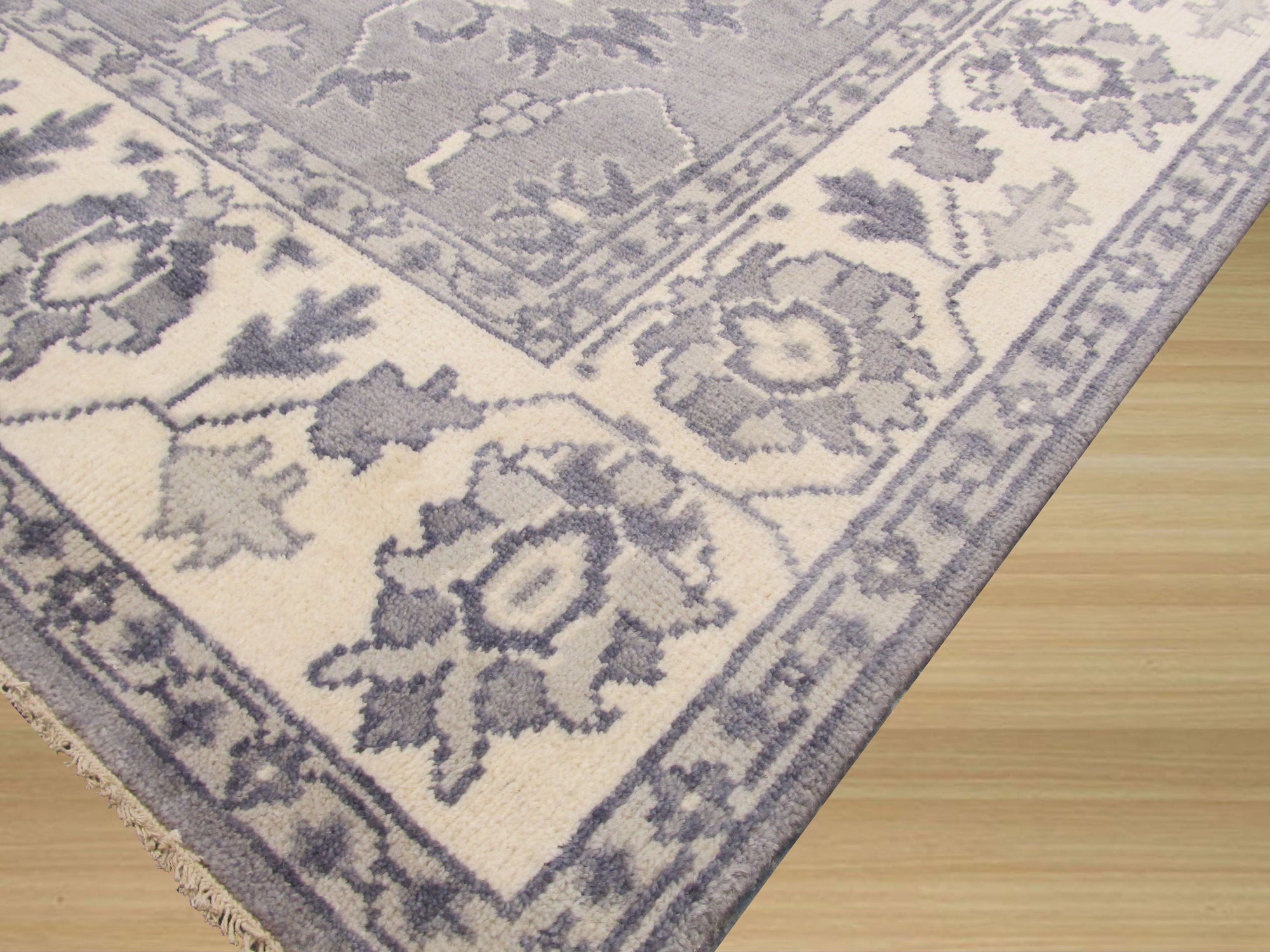 Beautiful Oriental Gray Hand Knotted Wool Rug, its intricate floral medallions and geometric borders rendered in subtle shades of gray and cream, laying elegantly on a polished hardwood floor.