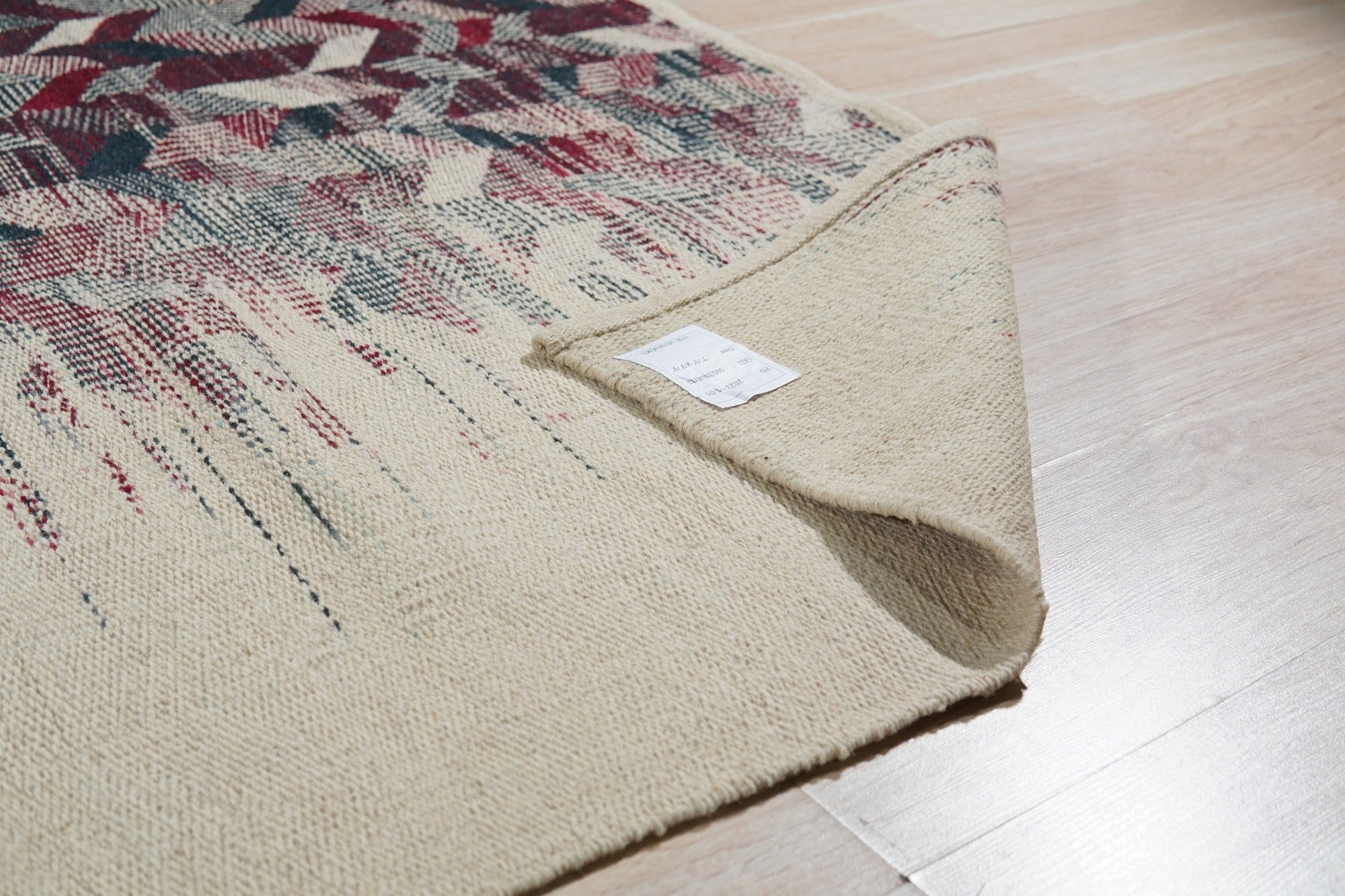 Brenda Refined Multicolor Flatweave Wool Rug, displaying a vibrant geometric pattern with warm reds, blues, and yellows, lies flat against a neutral floor, showcasing its intricate design and texture.