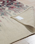 Brenda Refined Multicolor Flatweave Wool Rug, displaying a vibrant geometric pattern with warm reds, blues, and yellows, lies flat against a neutral floor, showcasing its intricate design and texture.