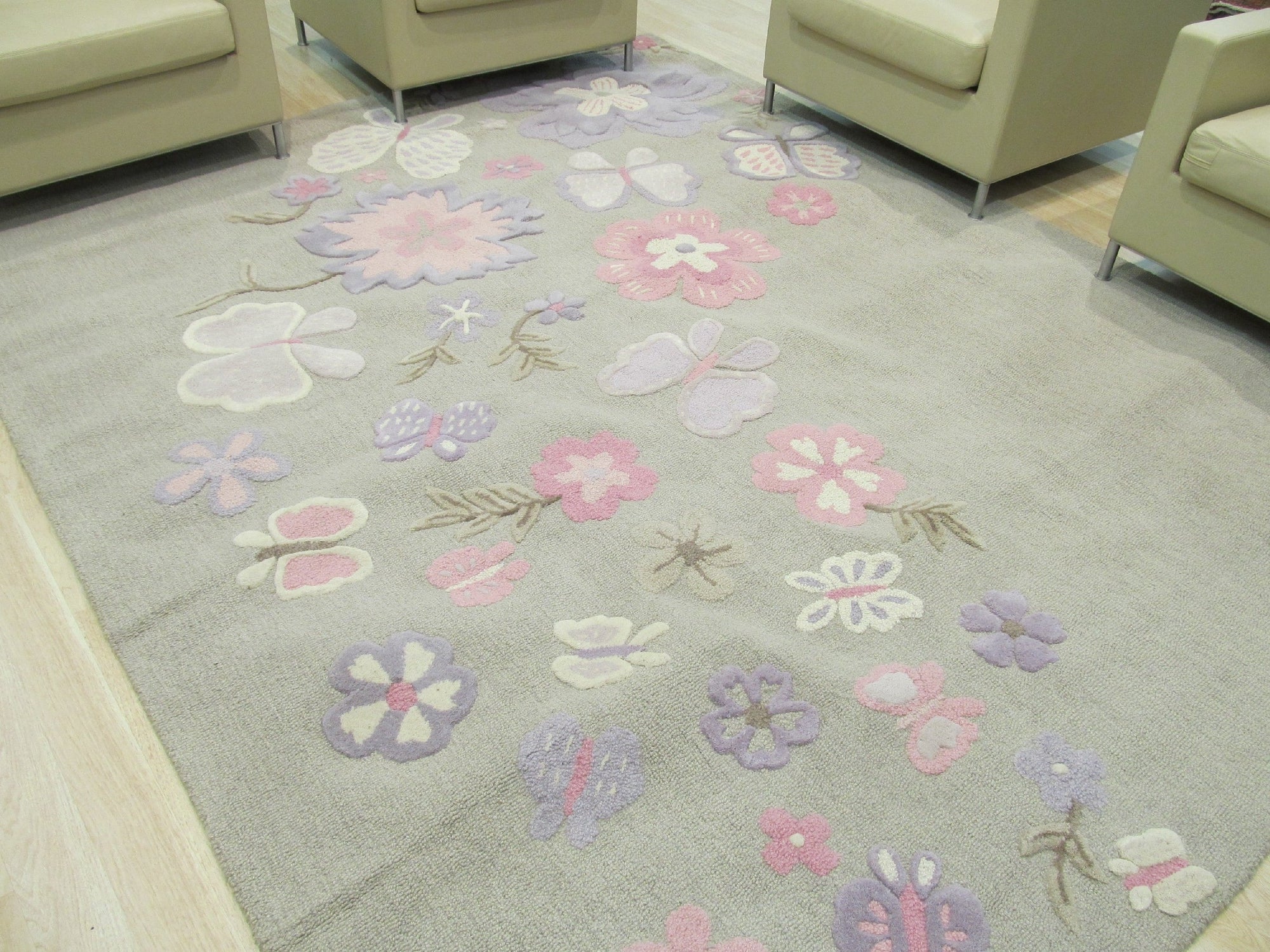 Rustic Elena Gray Hand Tufted Wool Rug, a soft gray wool rug with a subtle, distressed pattern, lies on a light wood floor, showcasing its hand-tufted texture and understated elegance in a room setting.