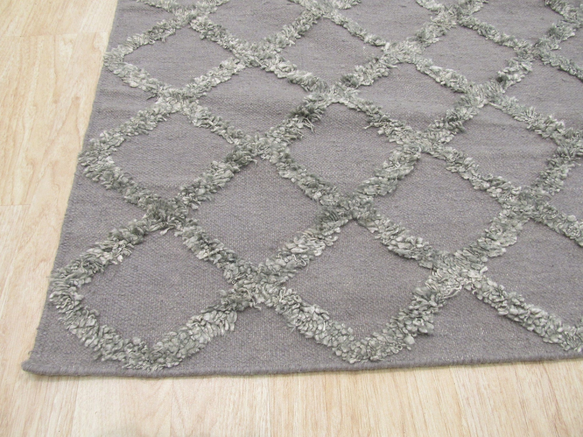 Nina Marrakesh Dark Gray Hand Knotted Wool & Viscose Rug, blending dark gray tones in a hand-knotted construction, displayed on a light hardwood floor and partially covered by a modern gray sofa.