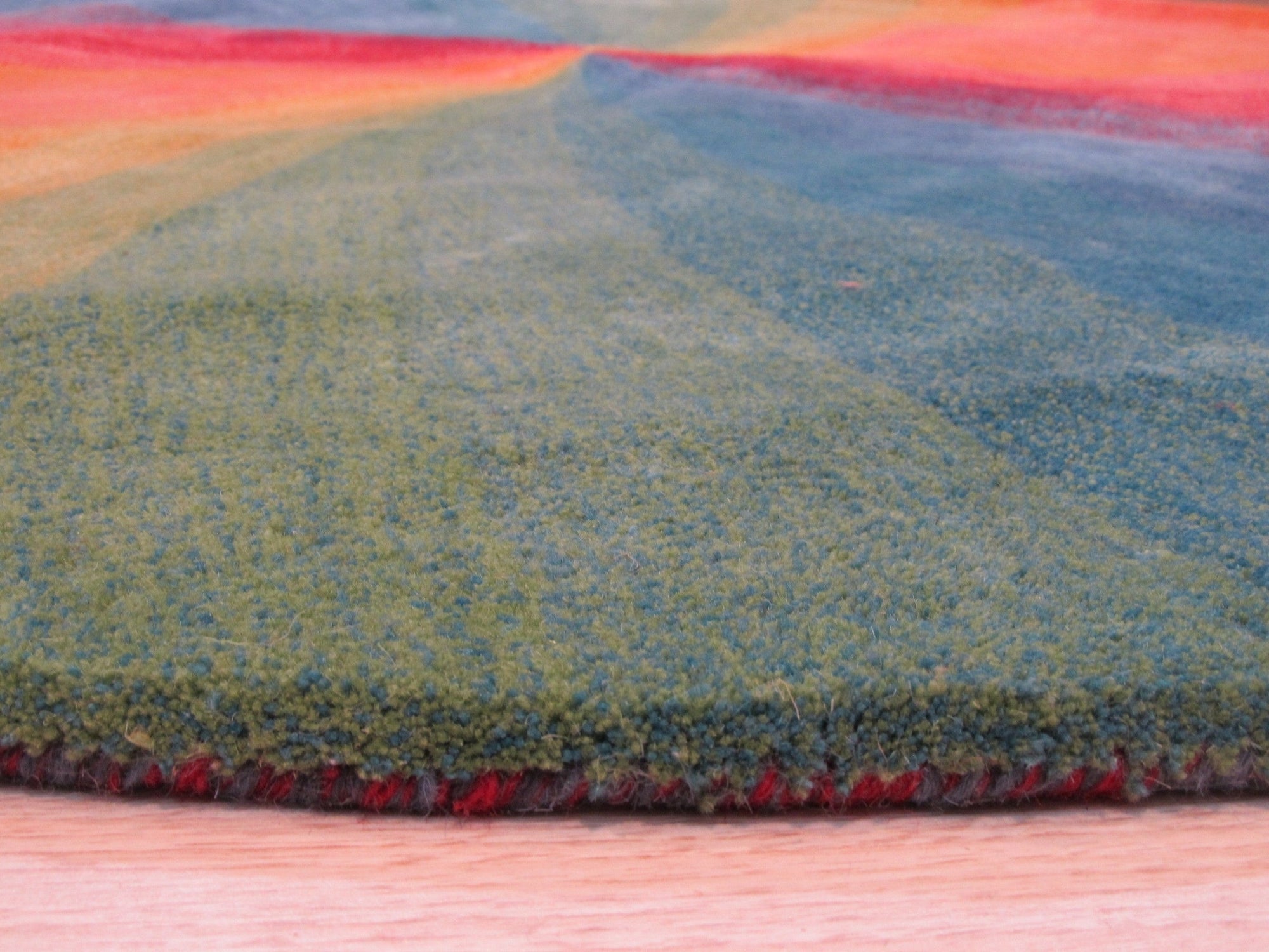 Talia Classic Rainbow Hand Tufted Wool Rug, bursts with vibrant hues in a contemporary living room setting. Wool construction showcases a dense, plush pile. Rainbow stripes cascade across the rug, adding playful energy to the space.
