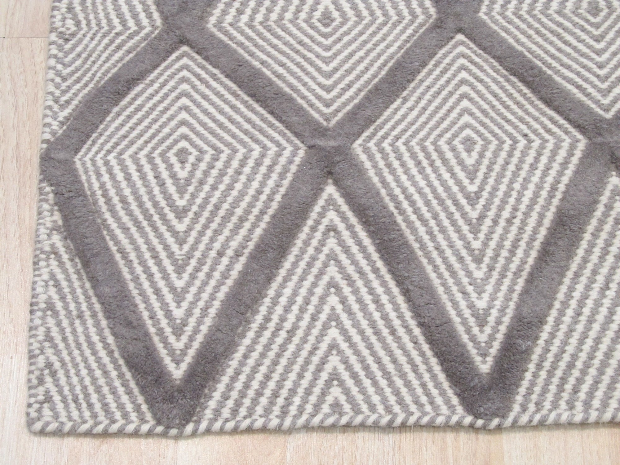 Trendy Diamond Gray Hand Knotted Wool Rug, its muted gray tones and diamond pattern subtly enhance a modern living room, seen under warm ambient light accentuating the rug's hand-knotted texture.