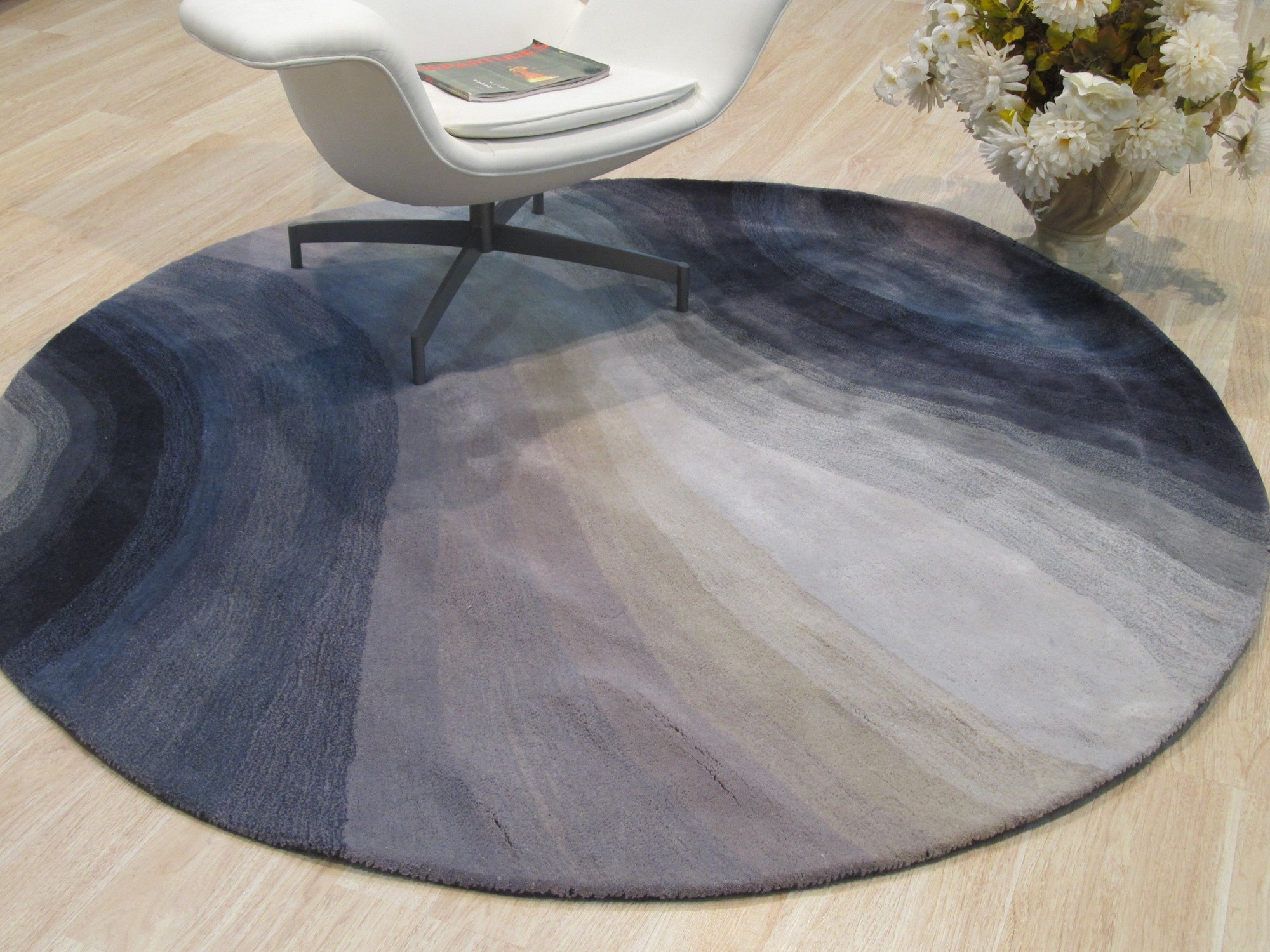 Xena Violet Blue Hand Tufted Wool Rug, its swirling violet and blue hues softening a bright, modern living room. The dense, hand-tufted wool adds texture and warmth to the space, complemented by clean lines and minimalist furniture.