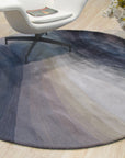 Xena Violet Blue Hand Tufted Wool Rug, its swirling violet and blue hues softening a bright, modern living room. The dense, hand-tufted wool adds texture and warmth to the space, complemented by clean lines and minimalist furniture.