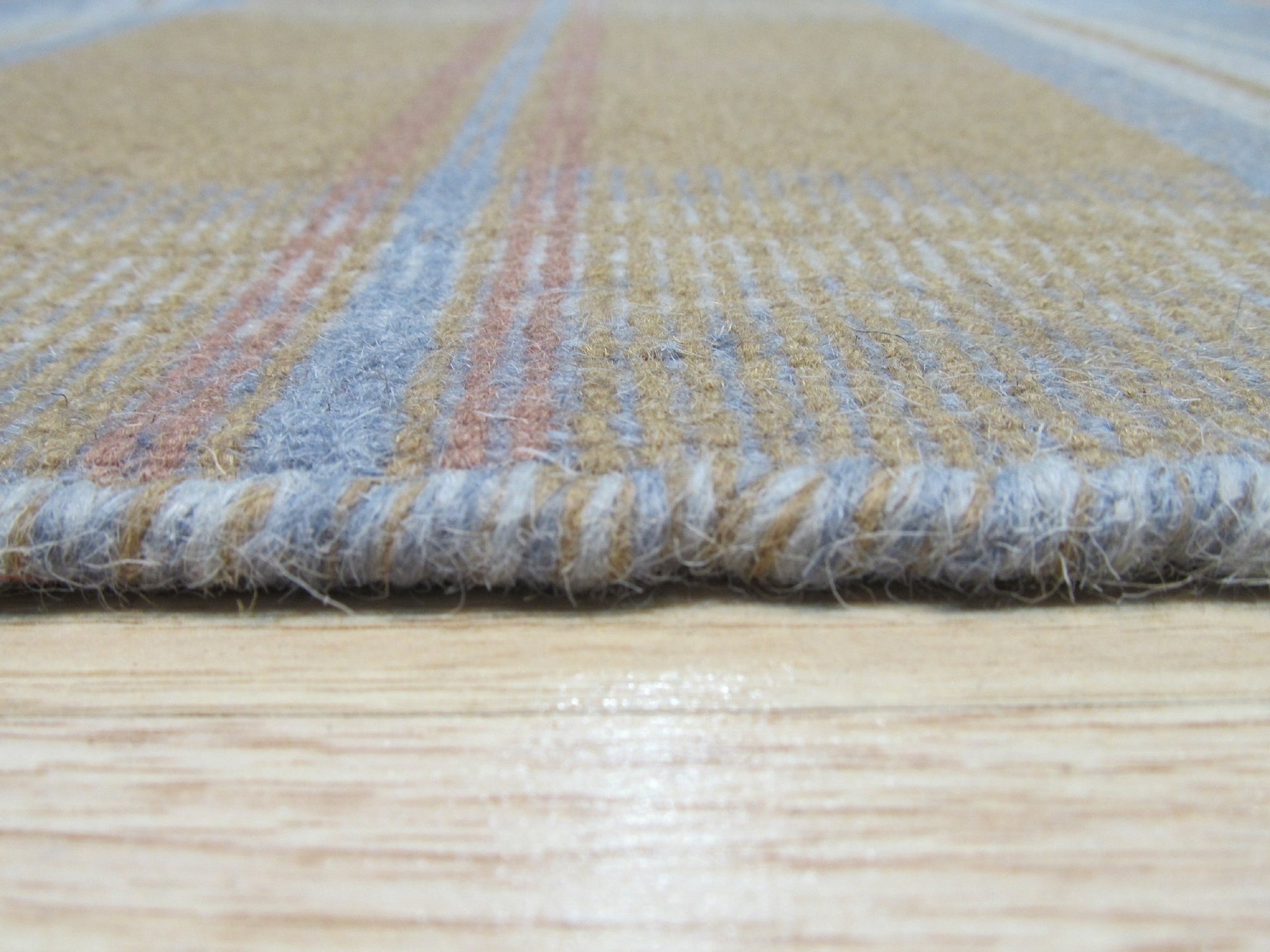 Sarrah Delicate Gold Flatweave Wool Rug graces a bright, airy living room. Sunlight highlights the rug's subtle gold tones and flatweave construction, complementing the room's modern aesthetic with its delicate pattern.