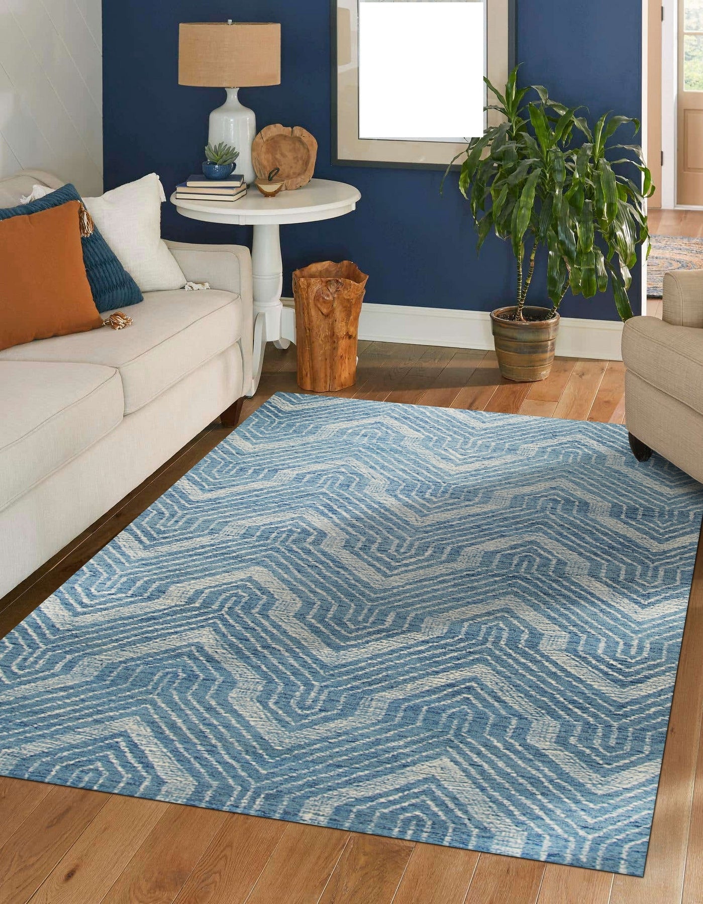 Lila Dahlia Blue Hand Tufted Wool Rug, showcasing swirling floral patterns in deep blues and creams against a lighter blue backdrop, seen on a light wood floor.