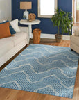 Lila Dahlia Blue Hand Tufted Wool Rug, showcasing swirling floral patterns in deep blues and creams against a lighter blue backdrop, seen on a light wood floor.