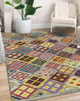 Nadia Kilim Multicolor Flatweave Wool Rug, sprawling across a sunlit living room floor; vibrant geometric patterns in reds, blues, and yellows energize the space, grounding a modern sofa and light wood coffee table.