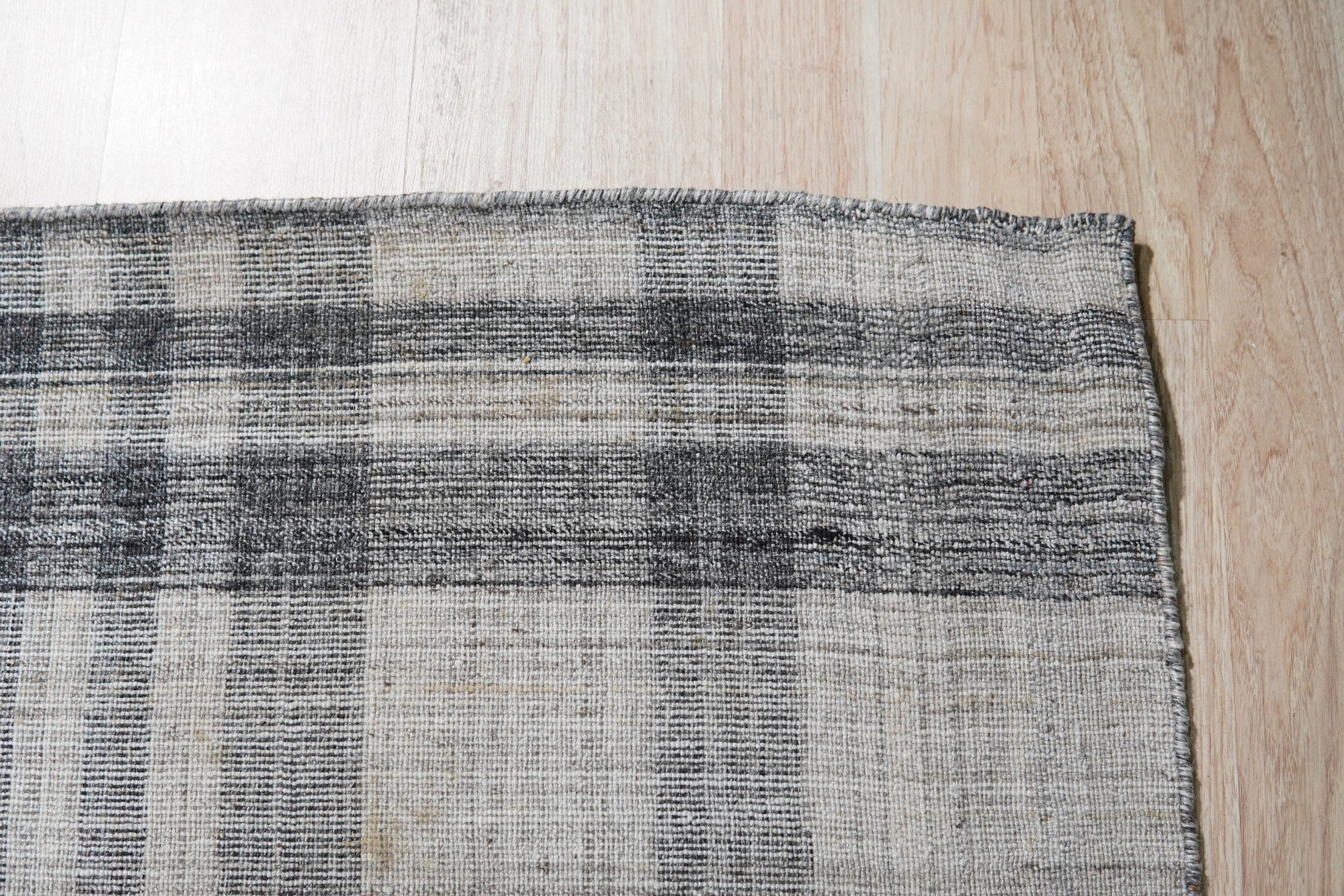Jasmine Stylish Gray Flatweave Wool Rug, with subtle geometric patterns in cool grays, anchors a modern living room. Light wood furniture and pops of green from potted plants complement the rug's understated elegance.
