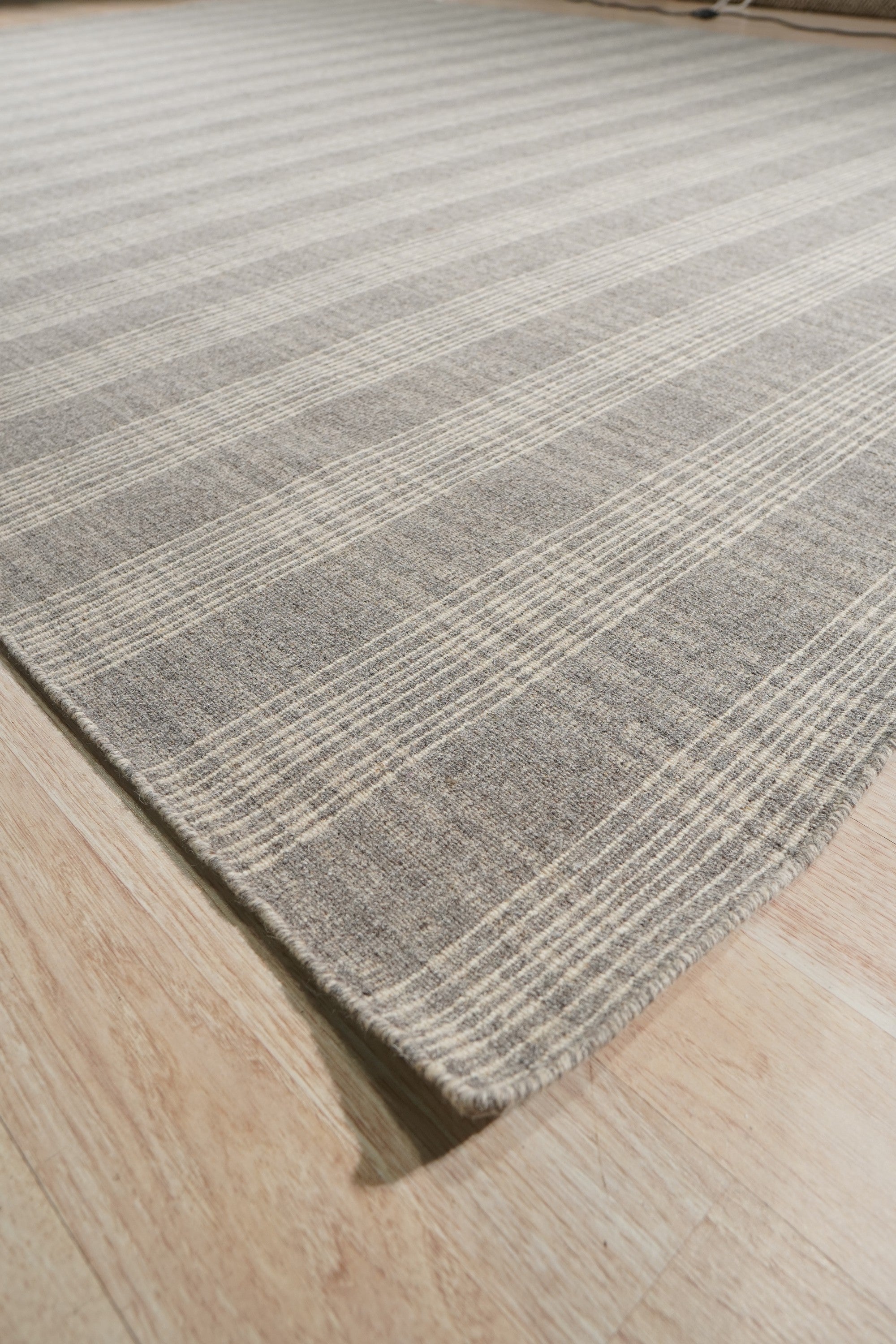 Classic Radiant Gray Flatweave Wool Rug, showcasing a subtle geometric pattern in shades of gray, lies flat on a light hardwood floor in a brightly lit living space.