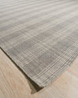 Classic Radiant Gray Flatweave Wool Rug, showcasing a subtle geometric pattern in shades of gray, lies flat on a light hardwood floor in a brightly lit living space.