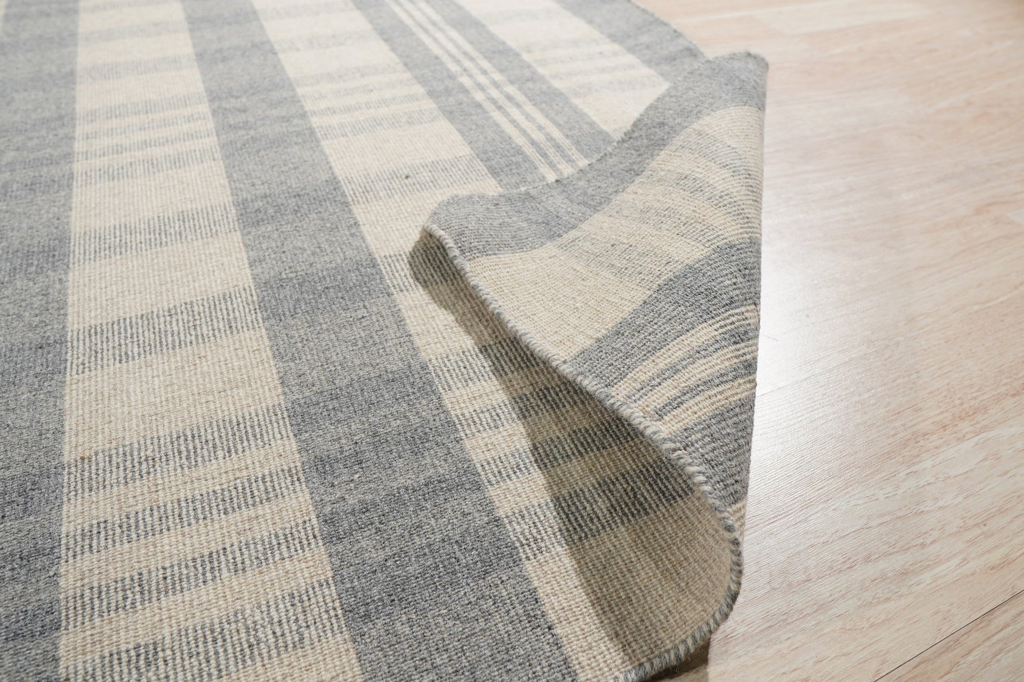 Handcrafted Vibrant Gray Flatweave Wool Rug, showcasing its flatweave construction and vibrant gray tones, sits in a bright living space, adding texture and subtle pattern to the hardwood floor.