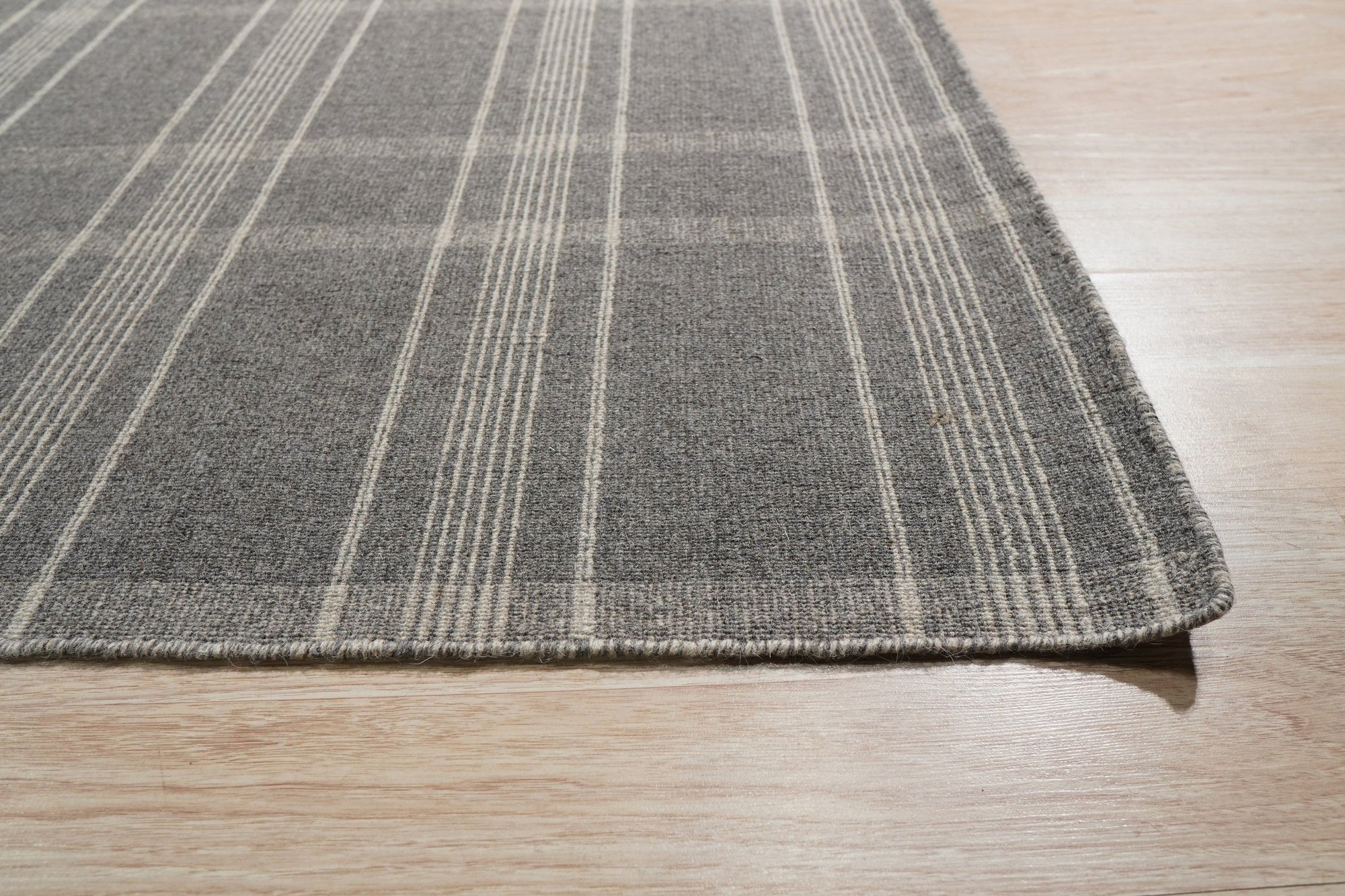 Graceful Quinn Gray Flatweave Wool Rug, showcasing a subtle geometric pattern in shades of gray, lies elegantly on a light-colored wood floor in a bright, minimalist room.
