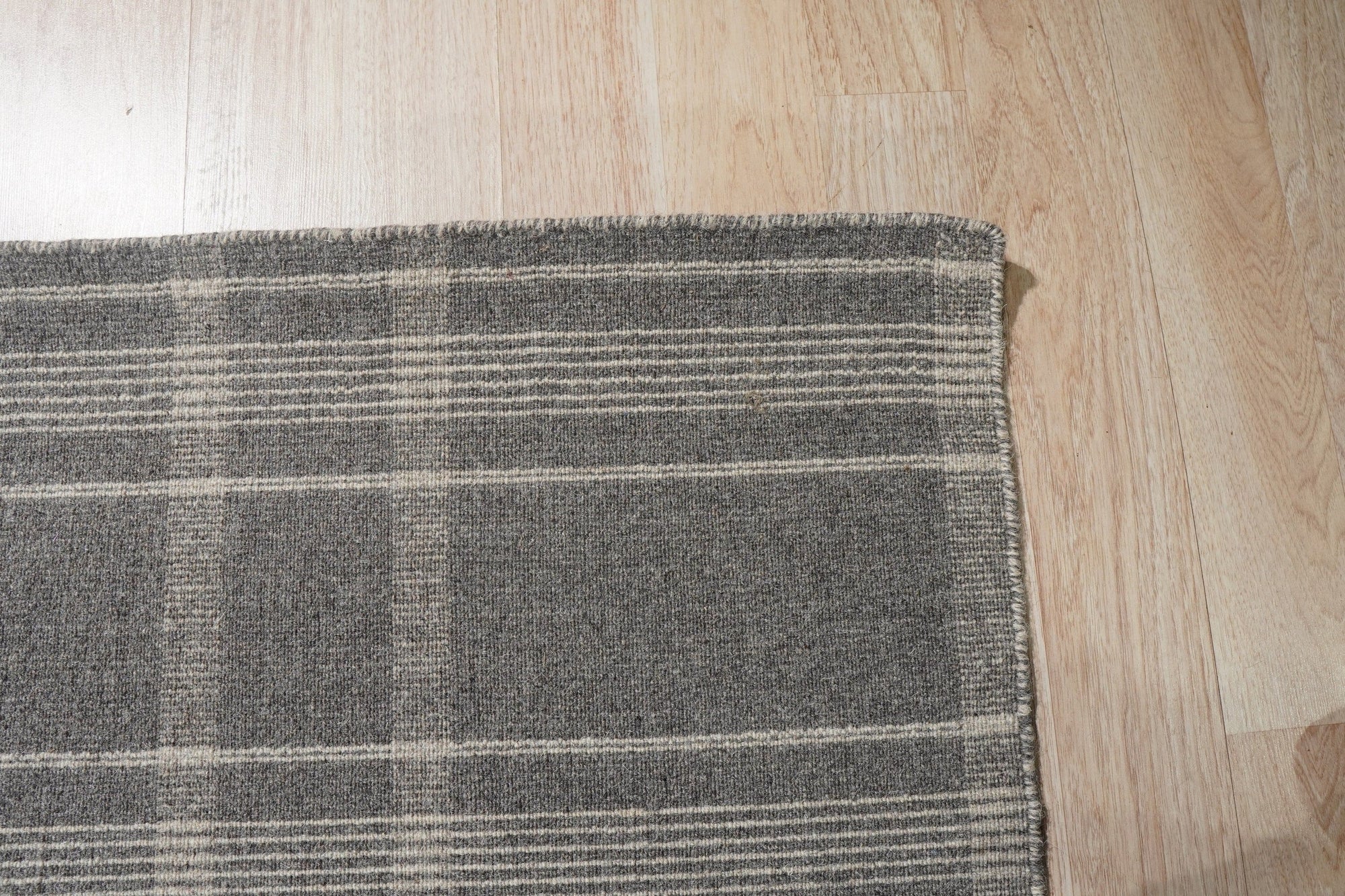 Graceful Quinn Gray Flatweave Wool Rug displayed in a bright living room setting. Its subtle gray tones and flatweave construction complement a modern, minimalist design with a light-colored sofa and coffee table.