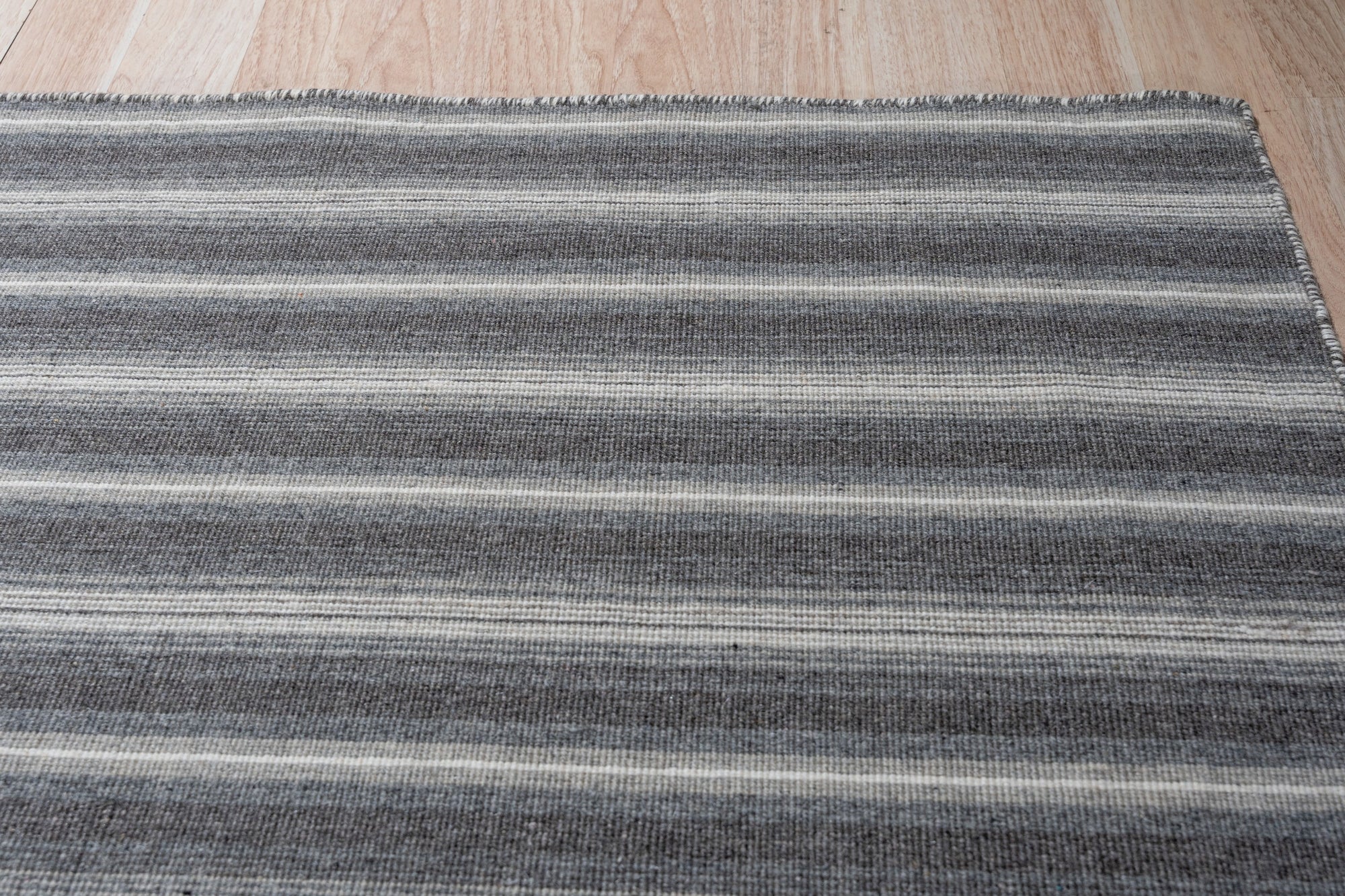 Lush Timeless Gray Flatweave Wool Rug, showcasing its subtle gray tones and flatweave construction, rests elegantly in a well-lit living space, complementing the neutral decor.