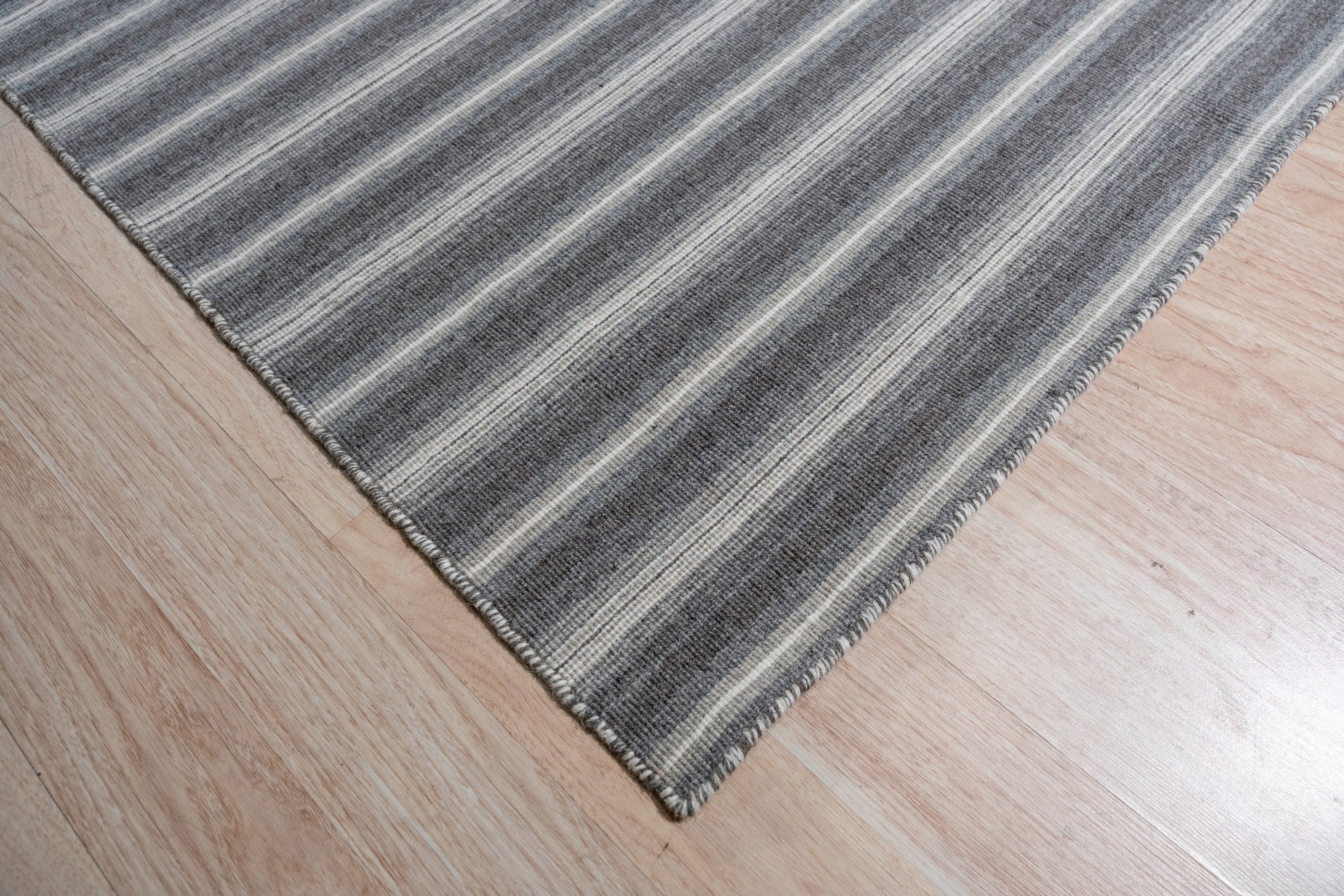 Lush Timeless Gray Flatweave Wool Rug, showcasing its subtle tonal variations in a bright, airy living room setting. The rug anchors a modern sofa and adds a touch of understated elegance to the polished wood floor.