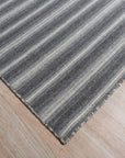 Lush Timeless Gray Flatweave Wool Rug, showcasing its subtle tonal variations in a bright, airy living room setting. The rug anchors a modern sofa and adds a touch of understated elegance to the polished wood floor.