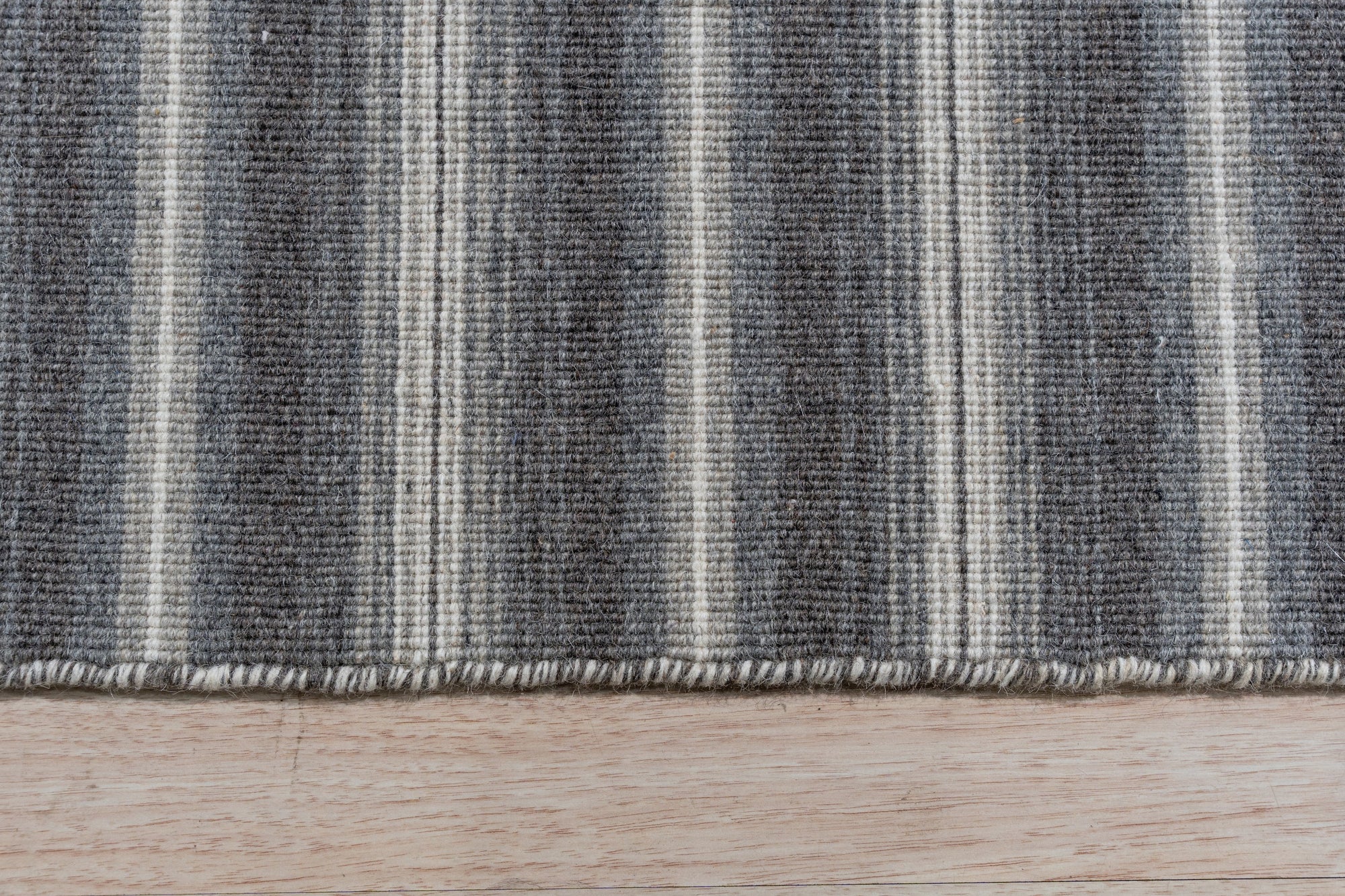 Lush Timeless Gray Flatweave Wool Rug, a gray wool rug with a subtly textured flatweave design, sprawls elegantly on a light hardwood floor, enhancing a modern living room setup with a sofa and minimalist decor.
