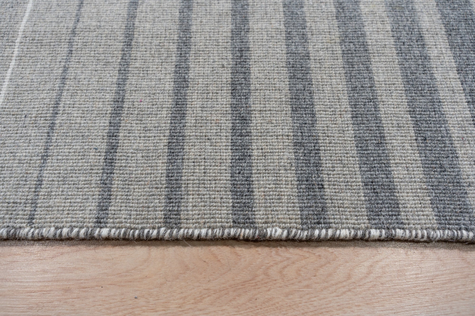 Timeless Comfortable Gray Flatweave Wool Rug lies elegantly on a hardwood floor, its subtle gray tones complementing a minimalist interior. Notice the flatweave construction allowing for a low profile, ideal for high-traffic areas, hinting at both durability and comfort.