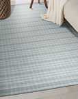 Timeless Celia Gray Flatweave Wool Rug, showcasing a geometric pattern in shades of gray and cream, laid on a light wood floor in a bright, modern living room setting.