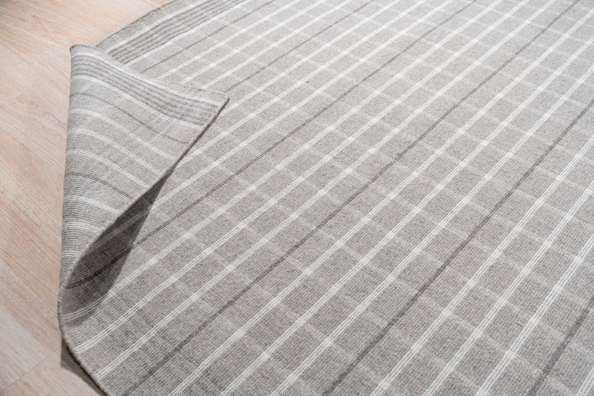 Timeless Celia Gray Flatweave Wool Rug, anchoring a bright, modern living room with its subtle geometric pattern and cool gray tones; potted plants and a mid-century modern chair complement its understated elegance.
